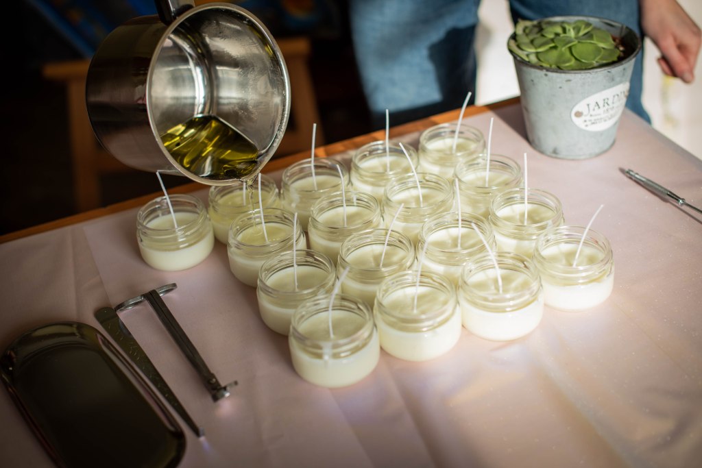 rows of white candles with long wicks and a jar pouring hot wax